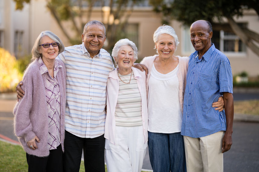 Portrait of cheerful senior people standing with arms around outside nursing home