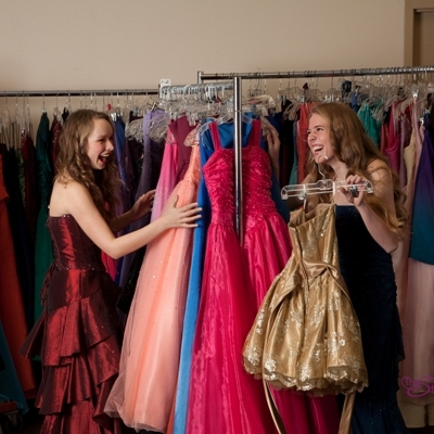 Two teens excitedly looking through Cinderella's Closet racks of gowns