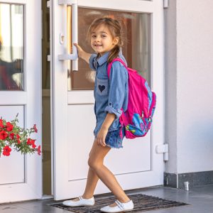 A little girl with a backpack, a schoolgirl opens the doors of the school.
