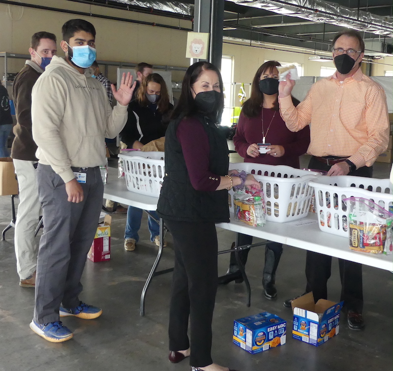 Volunteers waving while standing over food for kids at ALVN Weekend Food for Kids packing event