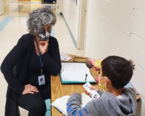A masked ALNV volunteer helping to tutor a young student
