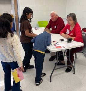 Children creating thank you cards at table with ALNV volunteers