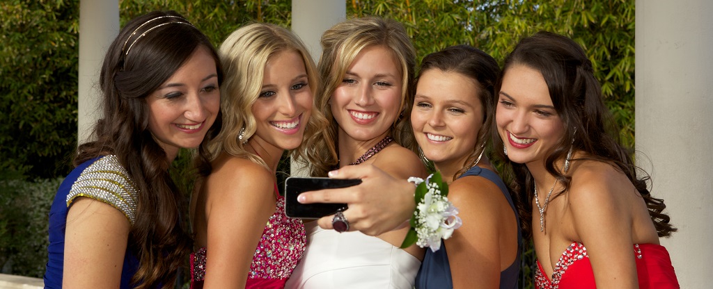 A group of five beautiful teenage girls dressed for the prom are taking a self portrait with a smart mobile phone.