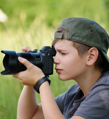 Boy with SLR camera shooting nature landscape in summer day in the village.