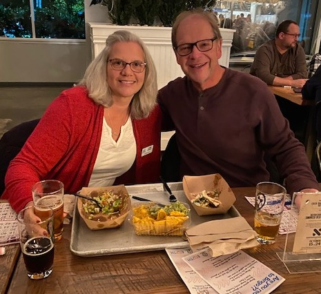 Two people sitting at a table with food and drinks